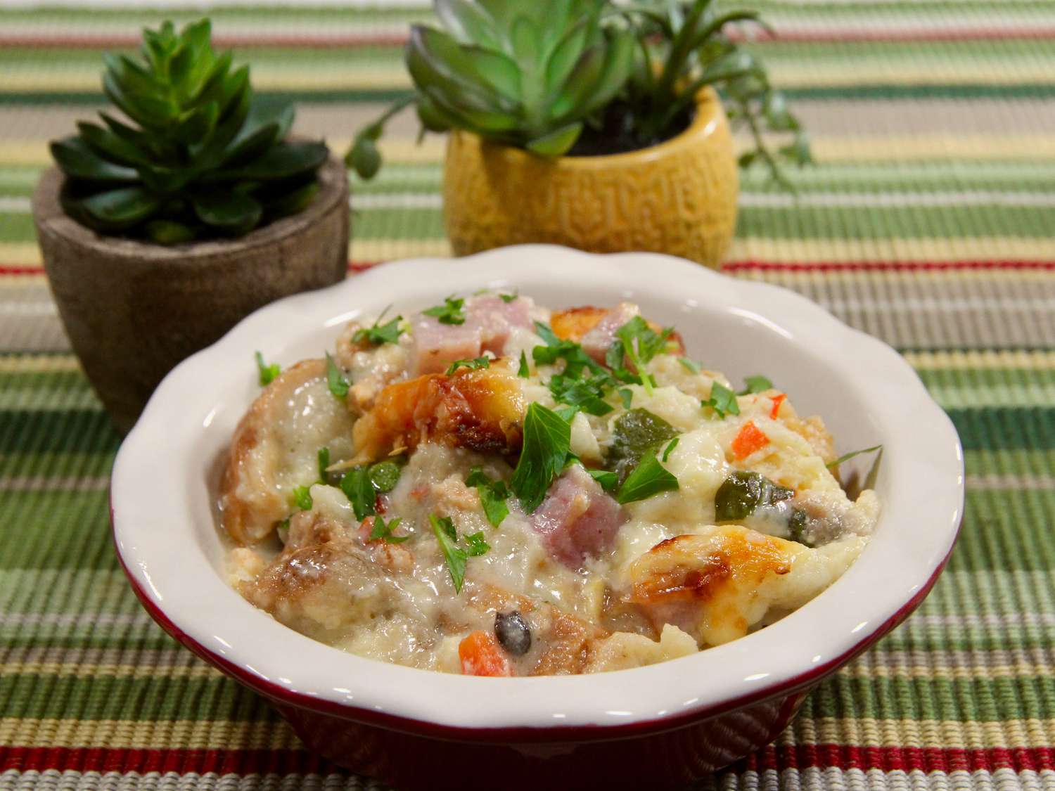 red bowl with mom's breakfast strata on green striped placemat with potted plants